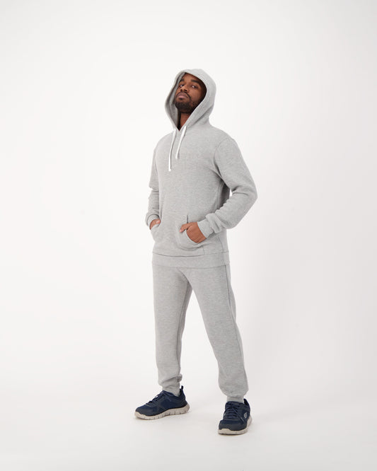 A stylish man wearing a grey unisex fleece hooded sweatshirt paired with matching sweatpants. The hooded sweatshirt, made of soft and cozy fleece fabric, offers both warmth and comfort. The grey color adds a versatile and contemporary aesthetic to the outfit. The man confidently dons this casual ensemble, showcasing a relaxed yet fashionable look. Perfect for lounging, workouts, or casual outings, this grey fleece hooded sweatshirt and sweatpants combination exudes both comfort and effortless style